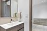 Wall-mounted mirror above a vanity featuring a wood-finish cabinet, white countertop, integrated rectangular sink, and polished chrome faucet