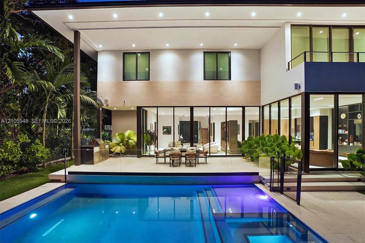 Contemporary two-story residence featuring expansive floor-to-ceiling glass wall panels, an integrated outdoor kitchen, a built-in swimming pool with 