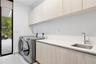 Laundry space featuring light-toned cabinetry, solid-surface countertops, an integrated stainless steel sink with a high-arch faucet, and full-height 
