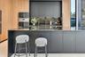 Modern kitchen featuring matte charcoal cabinetry, wood-finish paneling, an expansive island with a stone surface, built-in stainless steel appliances