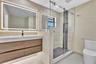 Floating wood-finish vanity with an integrated countertop, large LED-backlit mirror, and walk-in shower featuring glass enclosure, pebble stone floori