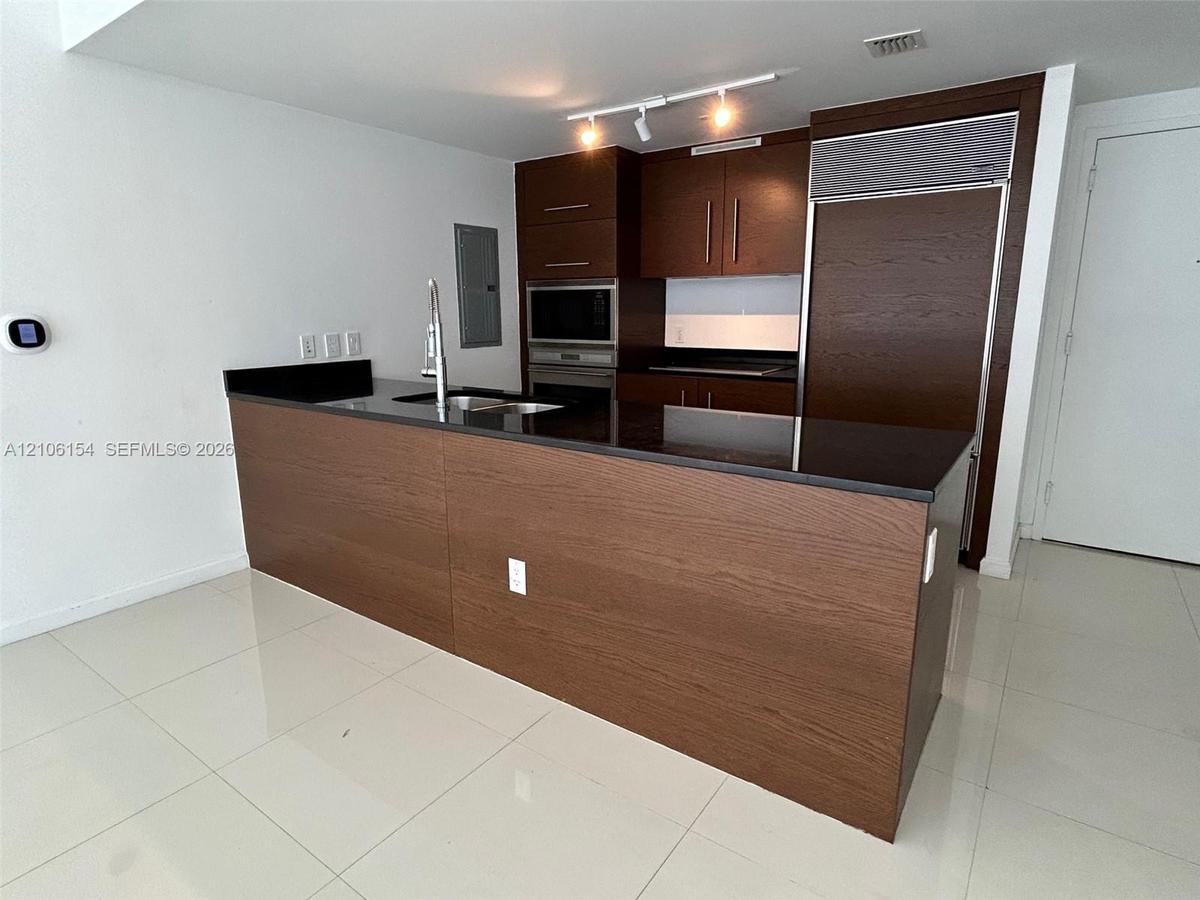 Kitchen featuring dark wood-finish cabinetry, black stone countertops, integrated stainless steel refrigerator, stainless steel built-in microwave and