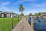 Waterfront property featuring a private composite dock, manicured lawn, exterior decorative post lighting, and direct canal access
