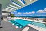 Rooftop pool featuring a structural pergola, light-toned stone decking, and a frameless glass perimeter railing