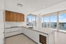 Kitchen featuring wood-finish upper cabinetry, white flat-panel lower cabinetry, light-toned stone-surface countertops, integrated wine refrigeration,