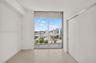 Floor-to-ceiling sliding glass doors, private balcony, neutral large-format tile flooring, and urban skyline backdrop