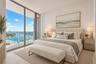 Floor-to-ceiling glass sliding doors opening to a private balcony with glass railing, complemented by neutral tile flooring