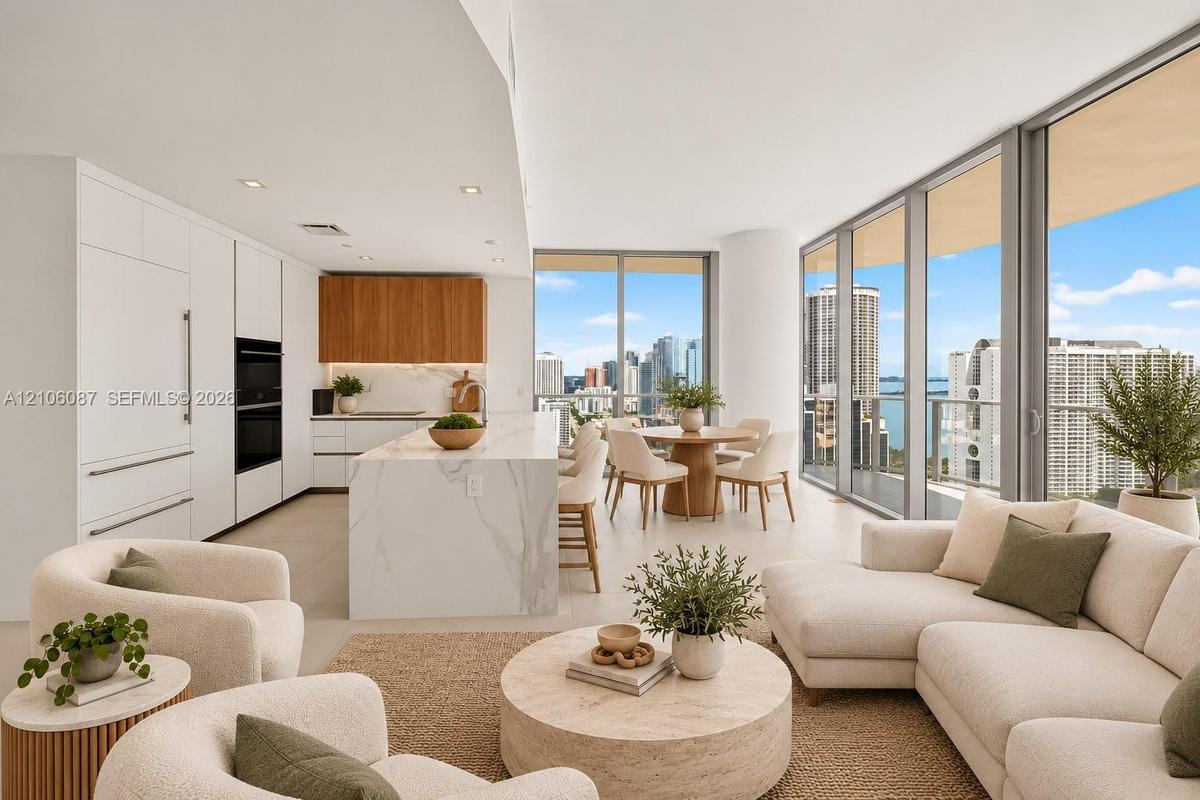 Open-concept kitchen featuring an oversized stone-topped waterfall island, custom flat-panel cabinetry, built-in appliances, and floor-to-ceiling wind