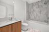 Wood-finish cabinetry, rectangular under-mount sink, stone-composite countertop, full-width mirror, and shower-tub combination with large-format tile 
