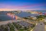 Aerial perspective featuring a waterfront coastline, bridge infrastructure, city skyline, and surrounding harbor