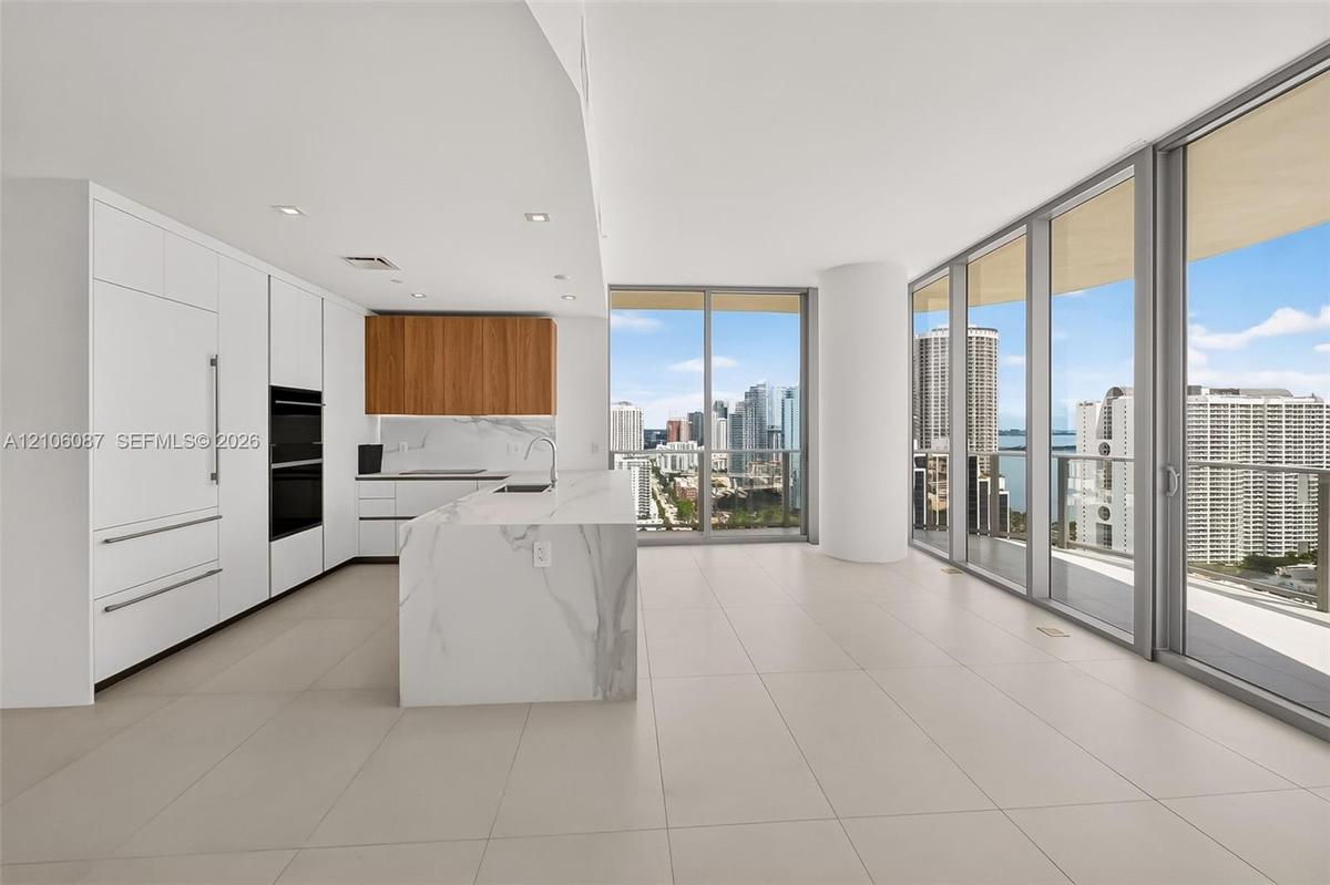 Kitchen featuring floor-to-ceiling cabinetry, a stone-surface island with waterfall edge, integrated appliances, wood-finish upper cabinets, and expan