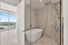 Freestanding soaking tub, floor-to-ceiling large-format tile wall surround, rain-style shower head with handheld attachment, glass-enclosed wet room, 