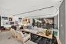 Open-concept space featuring light-toned wood-finish flooring, recessed track lighting, a built-in wet bar with dark stone-finish facing, and decorati
