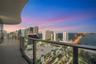 Curved balcony featuring large-format tile flooring and a glass-paneled railing overlooking an expansive urban skyline and waterfront