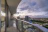 Covered balcony with a curvilinear roofline, glass panel railings, and tile flooring, featuring expansive urban surroundings