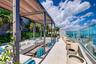 Rooftop terrace featuring a slatted metal pergola, light-toned tile flooring, glass panel perimeter railing, and integrated landscaping