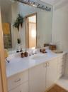 White vanity with integrated sink, chrome faucet, wall-mounted mirror, and overhead vanity lighting