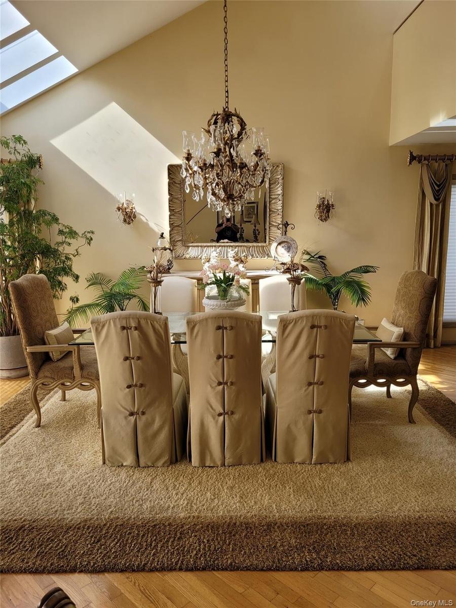 Vaulted ceiling with skylights, chandelier lighting, sconce lighting, mirror with ornate frame, and wood-finish flooring