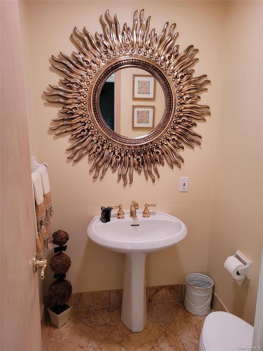 Elegant powder room featuring a pedestal sink with brass faucet, decorative sunburst mirror with gilt finish, tile flooring, and soft neutral wall ton