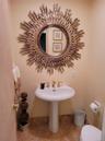 Elegant powder room featuring a pedestal sink with brass faucet, decorative sunburst mirror with gilt finish, tile flooring, and soft neutral wall ton