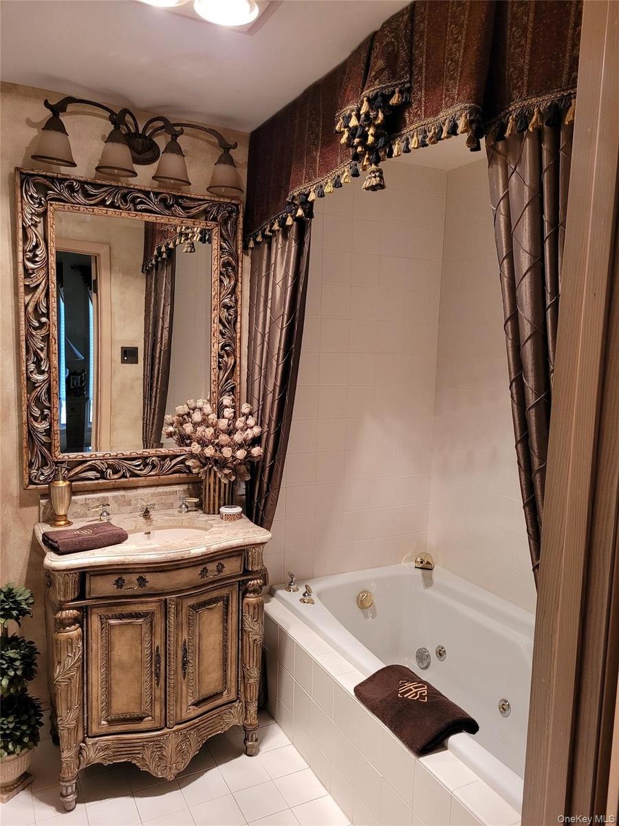 Jetted soaking tub, ornate carved wood-finish vanity, decorative mirror, and an antique bronze-finish light fixture