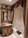 Jetted soaking tub, ornate carved wood-finish vanity, decorative mirror, and an antique bronze-finish light fixture