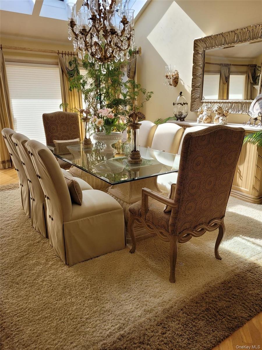 Dining area featuring a glass-top table, a substantial chandelier, skylights, and a large wall mirror with an ornate frame