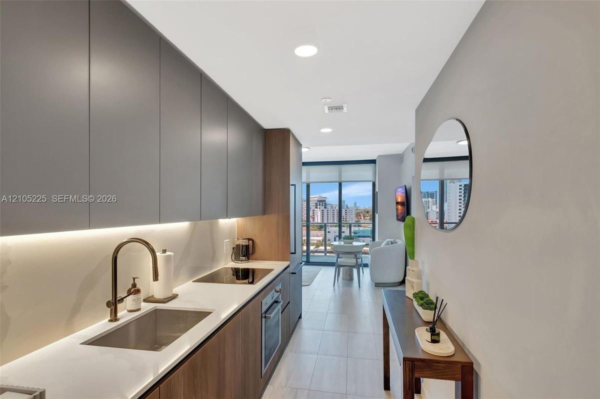 Galley kitchen featuring flat-panel cabinetry, integrated under-cabinet lighting, a built-in cooktop, and a stainless steel sink with a bronze-tone fa
