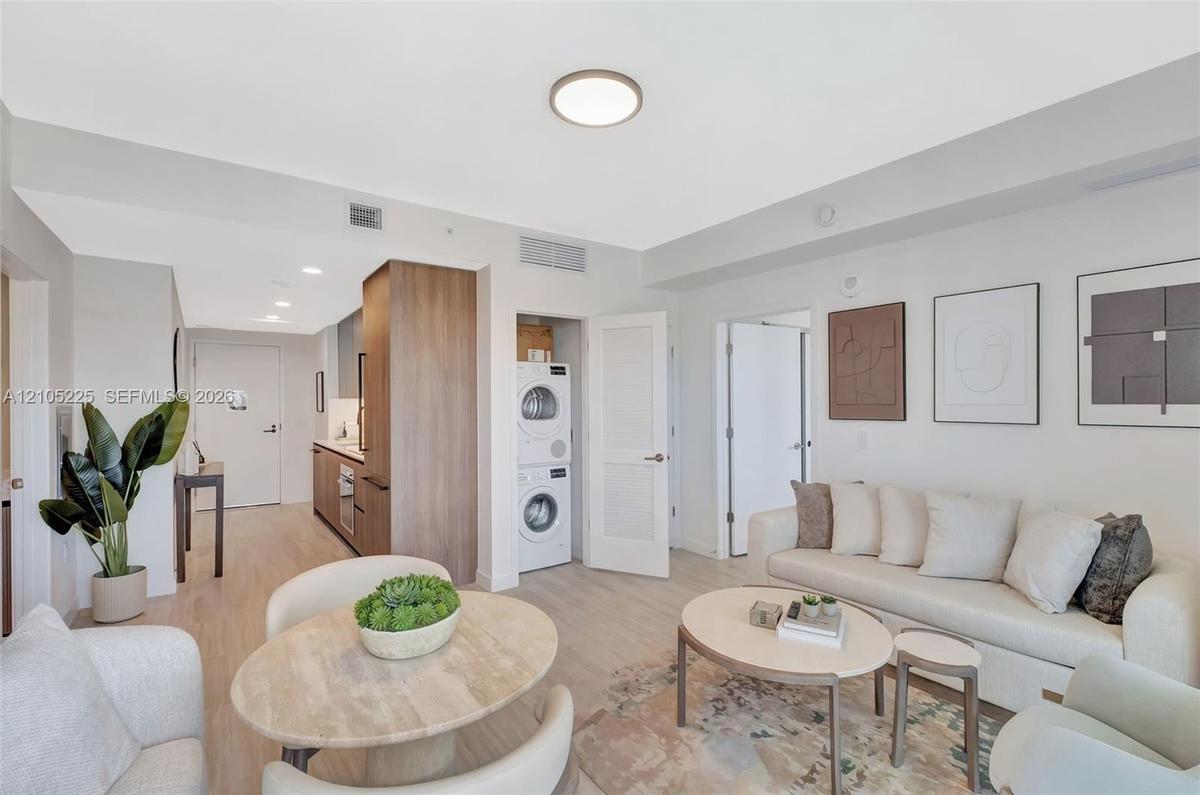 Open-concept living area with wood-finish flooring, recessed lighting, and a built-in stacked washer and dryer