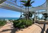 Expansive outdoor terrace featuring wood-finish decking, a white slatted pergola, lush landscaping, and a clear glass railing
