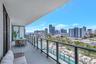 Covered balcony featuring concrete flooring, a glass and metal railing system, and city skyline scenery