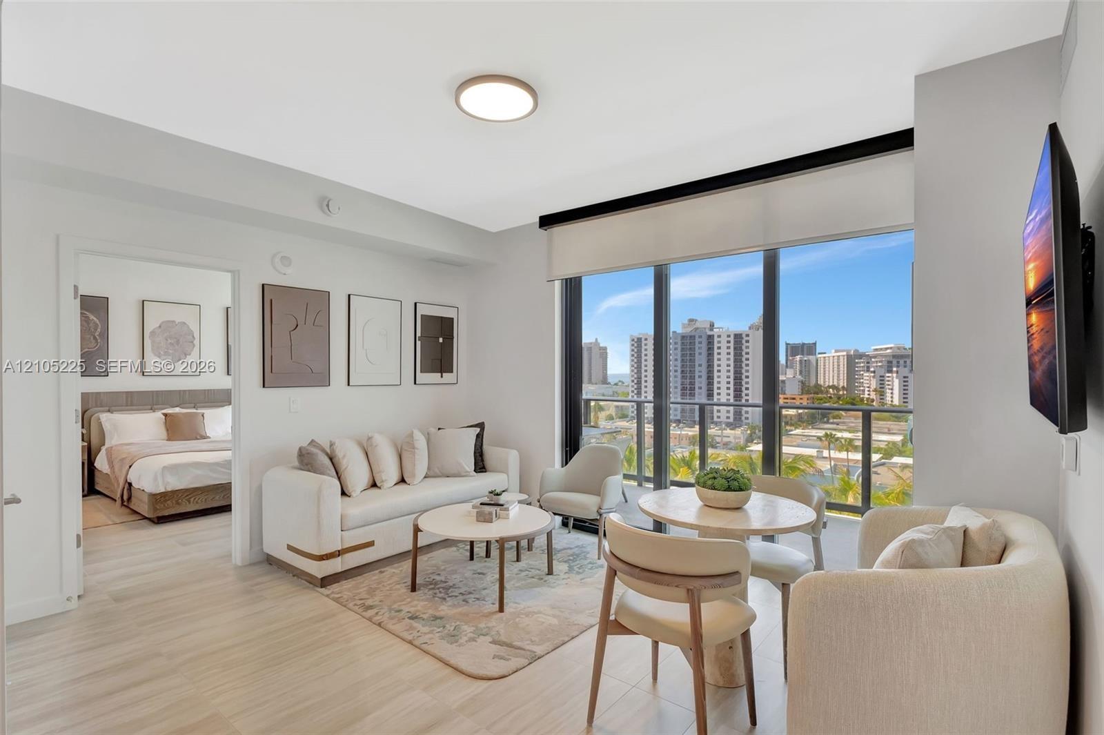 Expansive window wall with urban scenery, light wood-finish flooring, recessed ceiling light, and a dedicated dining area