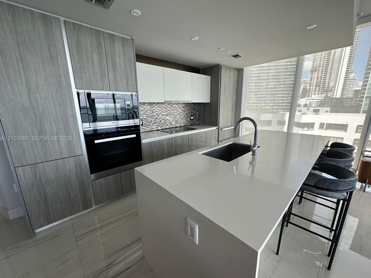 Kitchen featuring a central quartz-top island with an integrated sink, custom wood-finish cabinetry, built-in stainless steel appliances, and floor-to