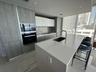 Kitchen featuring a central quartz-top island with an integrated sink, custom wood-finish cabinetry, built-in stainless steel appliances, and floor-to