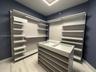 Custom storage system featuring adjustable shelving, integrated linear lighting, a central display island with a glass top, and stone-finish flooring