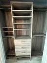Custom storage system featuring wood-finish cabinetry, built-in shelving, three integrated drawers with metallic pulls, and stainless steel hanging ro