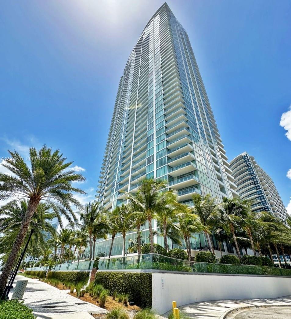 High-rise structure featuring floor-to-ceiling glass paneling, extensive wraparound balcony tiers, and contemporary glass railing systems, set against