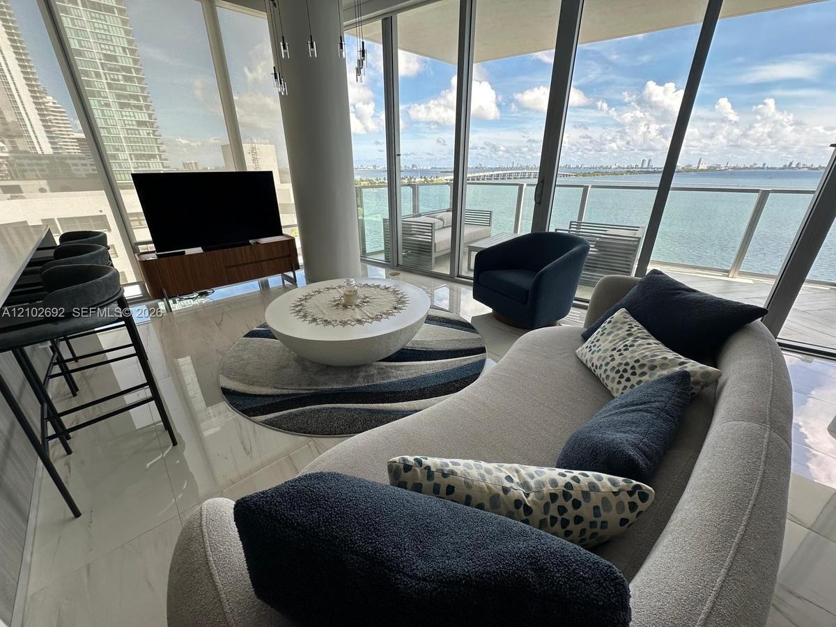Floor-to-ceiling windows, polished light-toned flooring, cylindrical architectural column, and expansive balcony with glass railings