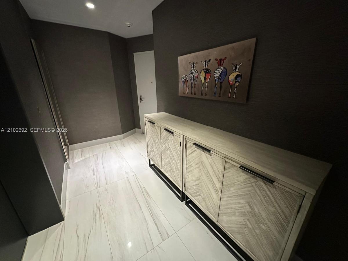 Entryway featuring large-format light-toned tile flooring, deep charcoal-colored wall coverings, and recessed ceiling lighting