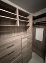 Built-in closet system featuring wood-finish cabinetry, multi-tier open shelving, integrated dresser drawers, brushed metal hardware, and a hanging ro