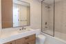 Modern vanity with wood-finish cabinetry, integrated countertop with rectangular basin, matte black plumbing fixtures, glass-enclosed shower, and mosa
