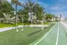 Outdoor fitness area featuring a synthetic running track, multi-use exercise frames, manicured landscaping with mature palms, and tiered retaining wal