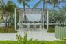 Outdoor patio featuring white tile flooring, a structured wooden pergola with an integrated ceiling fan, and surrounding tropical landscaping