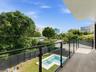 Balcony featuring light-toned tile flooring and a glass railing with a dark metal frame, overlooking a rear yard with an in-ground swimming pool and p