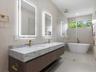 Floating dual-sink vanity with stone countertop, brass-finish fixtures, dual LED-backlit mirrors, freestanding soaking tub, and glass-enclosed walk-in