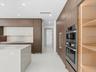 Modern kitchen featuring full-height wood-finish cabinetry, a stone-surfaced waterfall island, integrated stainless steel double wall ovens, and illum
