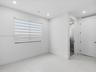 Neutral-toned interior featuring large-format tile flooring, recessed ceiling lighting, a single window with horizontal privacy blinds, and a solid-co