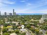Aerial perspective showcasing a flat-roofed modern residence with an expansive landscape, dense mature tree canopy, and proximity to the coastline