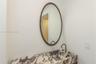 Stone countertop with an integrated basin, oval wall-mounted mirror with a bronze-toned frame, and a bronze-toned gooseneck faucet