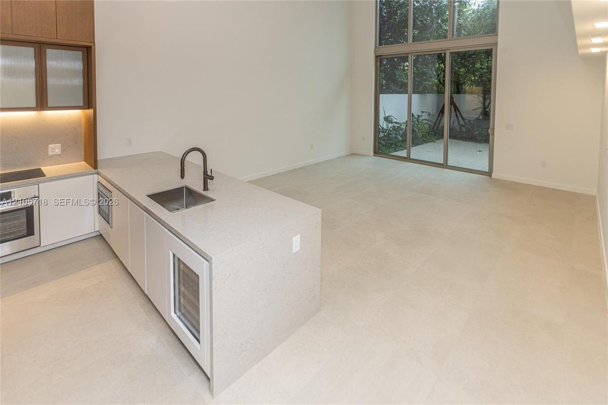 Kitchen featuring a stone-surface island, built-in wine refrigeration, high-ceiling glass sliding doors, and large-format tile flooring